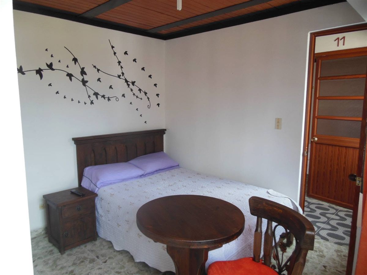 Habitación sencilla con cama doble, mesa redonda de madera con silla y mesa de noche